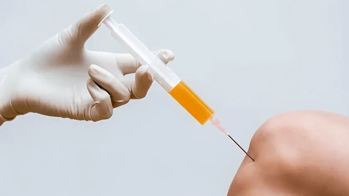 Mão com luva cirúrgica posicionando uma seringa para aplicação na região do joelho
